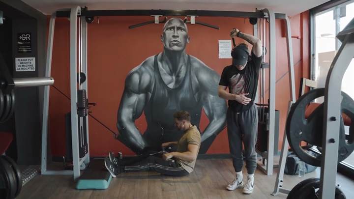 Two members training at the cable machine in front of the painted wall.